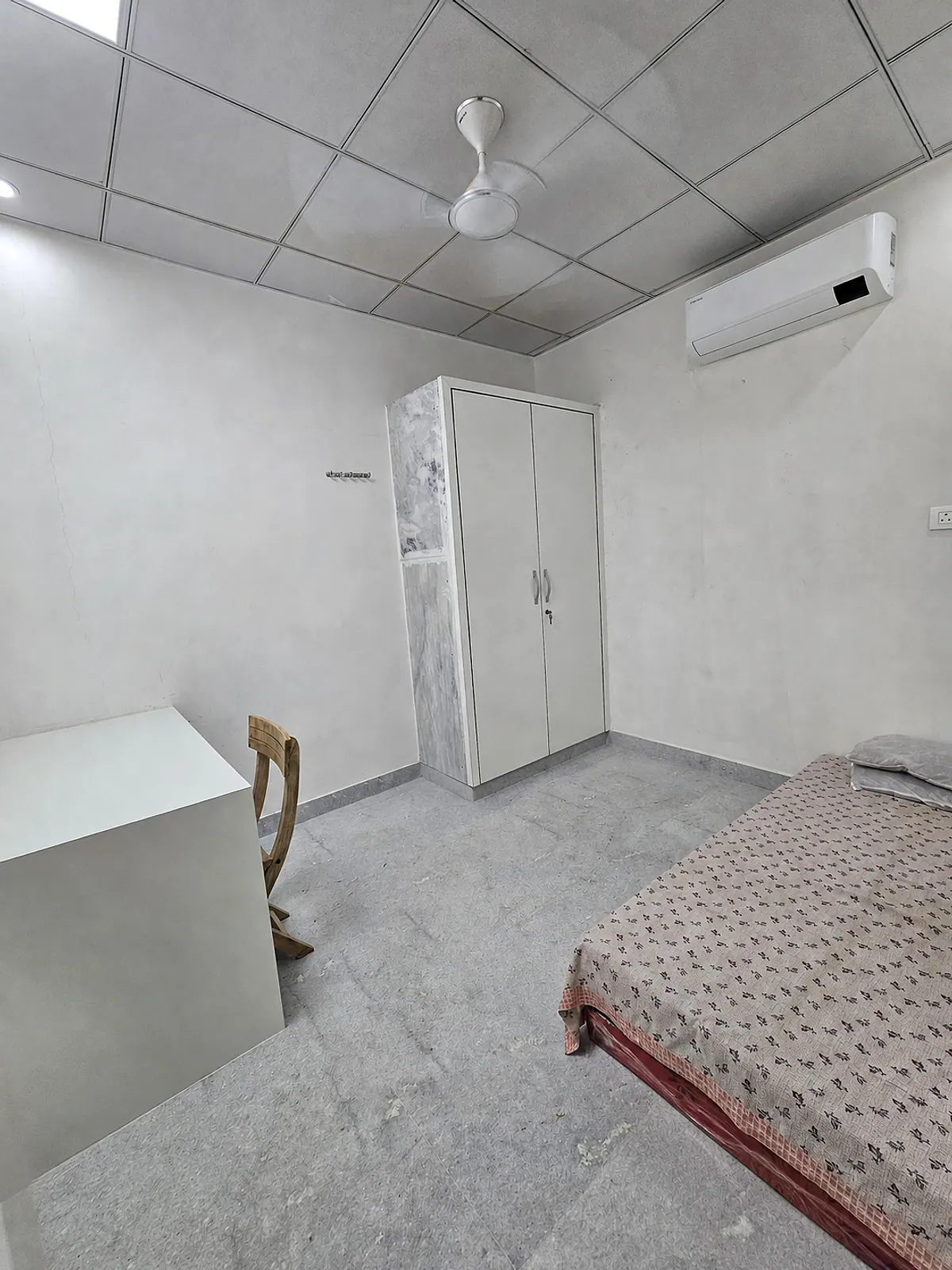 Another real view of the furnished room with a bed, study desk, wardrobe, ceiling fan and split air conditioner